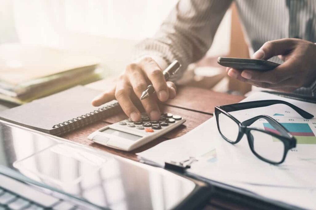 Businessman calculating project costs using a calculator and phone, focused on financial analysis.