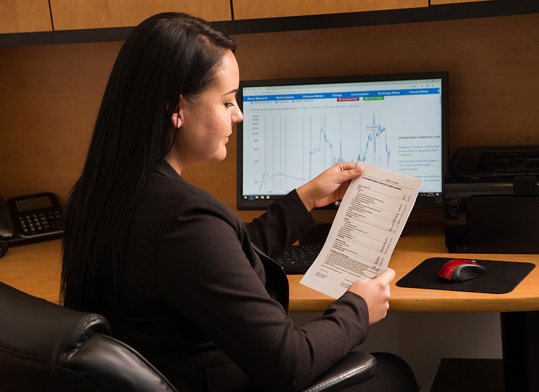 A woman dressed in a suit operating her system while looking at document